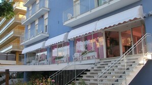 Un hotel de varios pisos con balcones, mobiliario exterior y una escalera que lleva a la entrada.