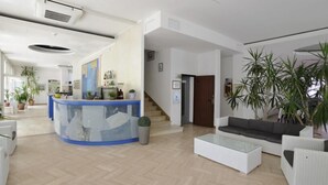 Un vestíbulo amplio con un mostrador de recepción, una escalera y una zona de estar con sofá y mesa de centro.