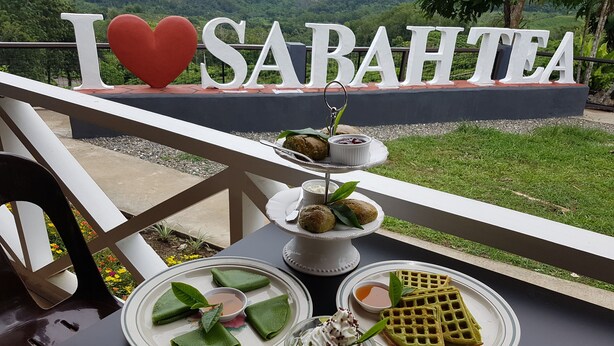A table with a variety of desserts and a sign that reads "I love Sabahtea" in the background. - Sabah Tea Resort (Ranau)