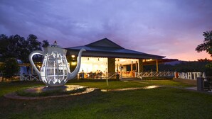 A building with a covered outdoor seating area and a large teapot sculpture in the foreground. - Sabah Tea Resort (Ranau)
