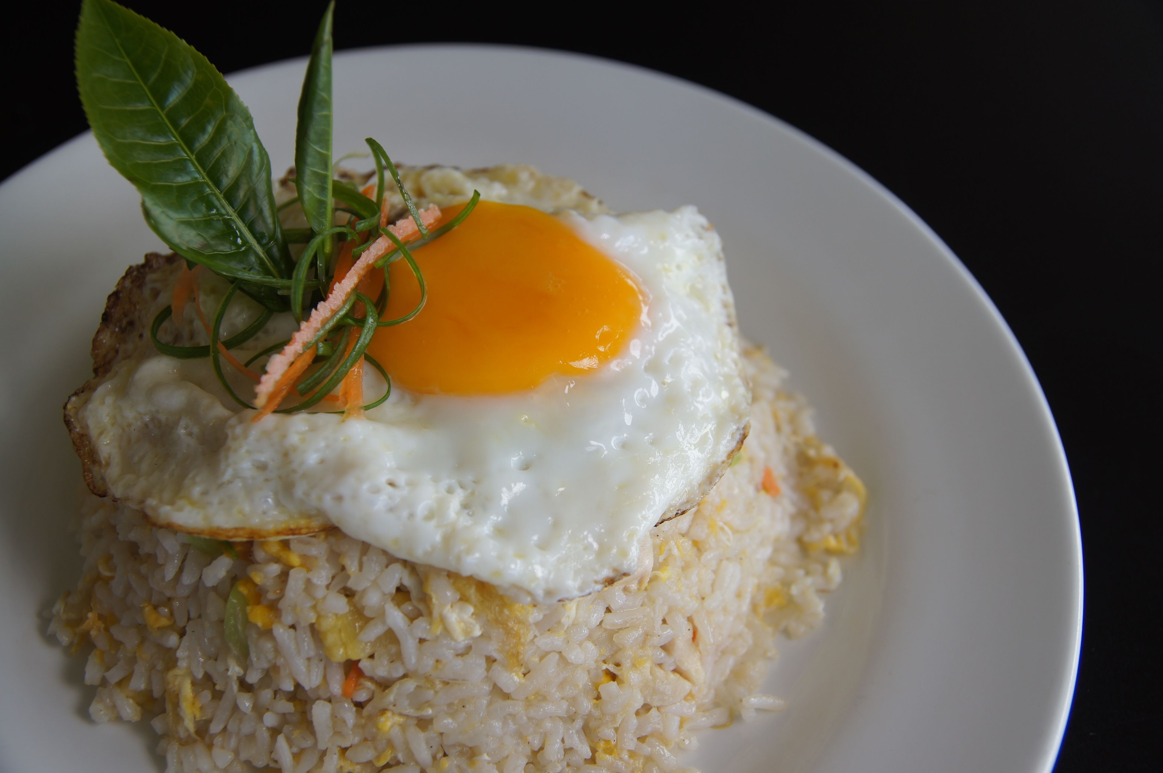 A plate of fried rice topped with a fried egg and garnished with green leaves and carrot strips.