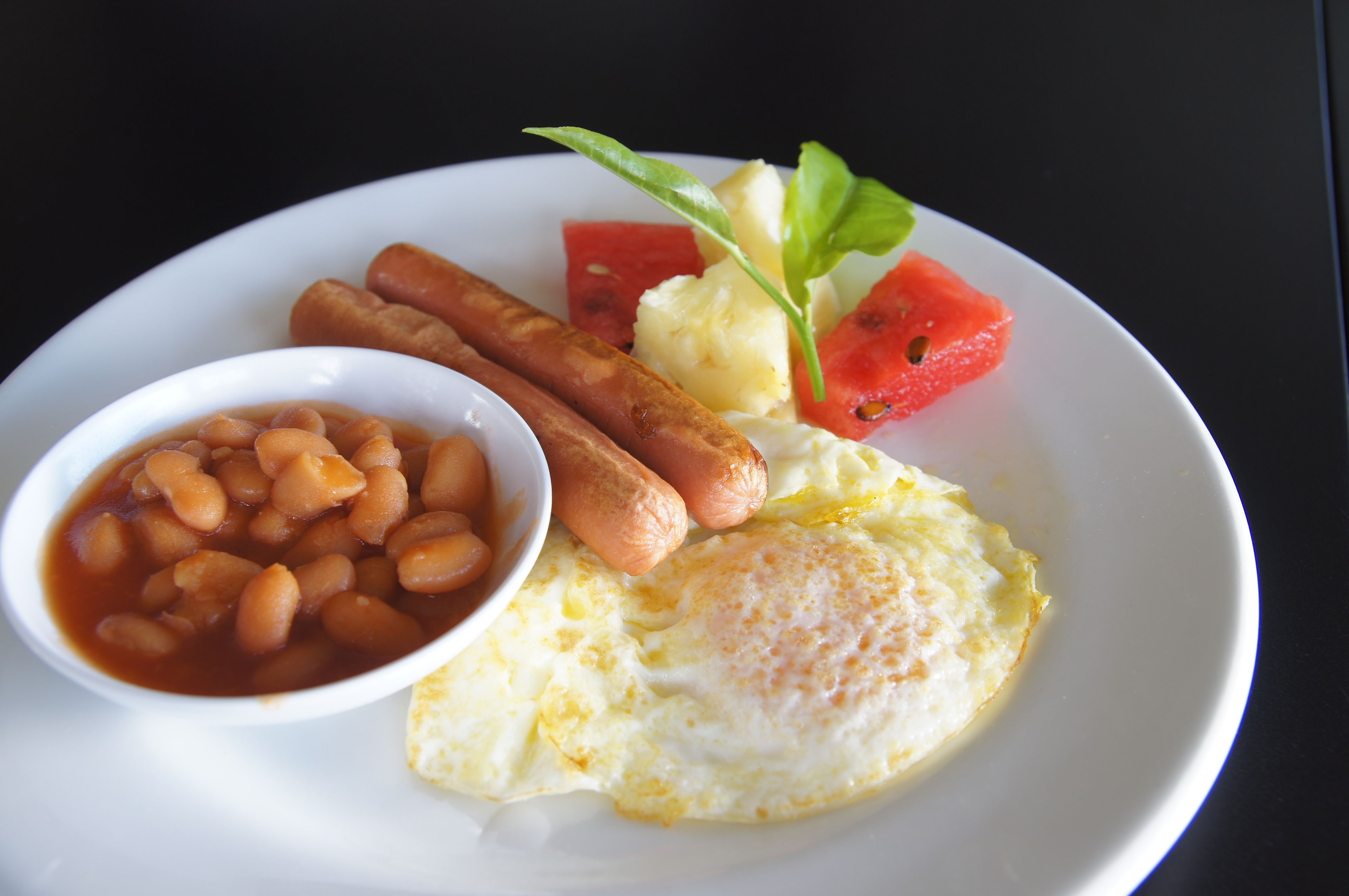 A plate with beans, sausages, a fried egg, and watermelon.