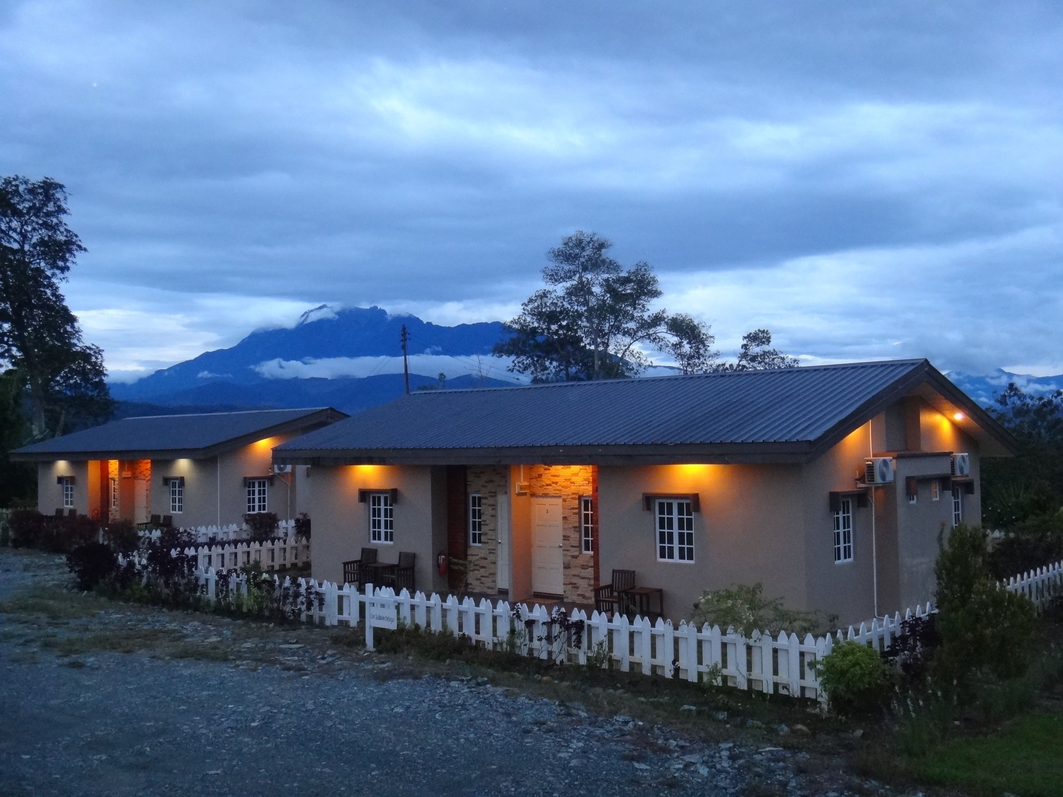 A two-story building with a white picket fence, stone accents, and a mountain backdrop.
