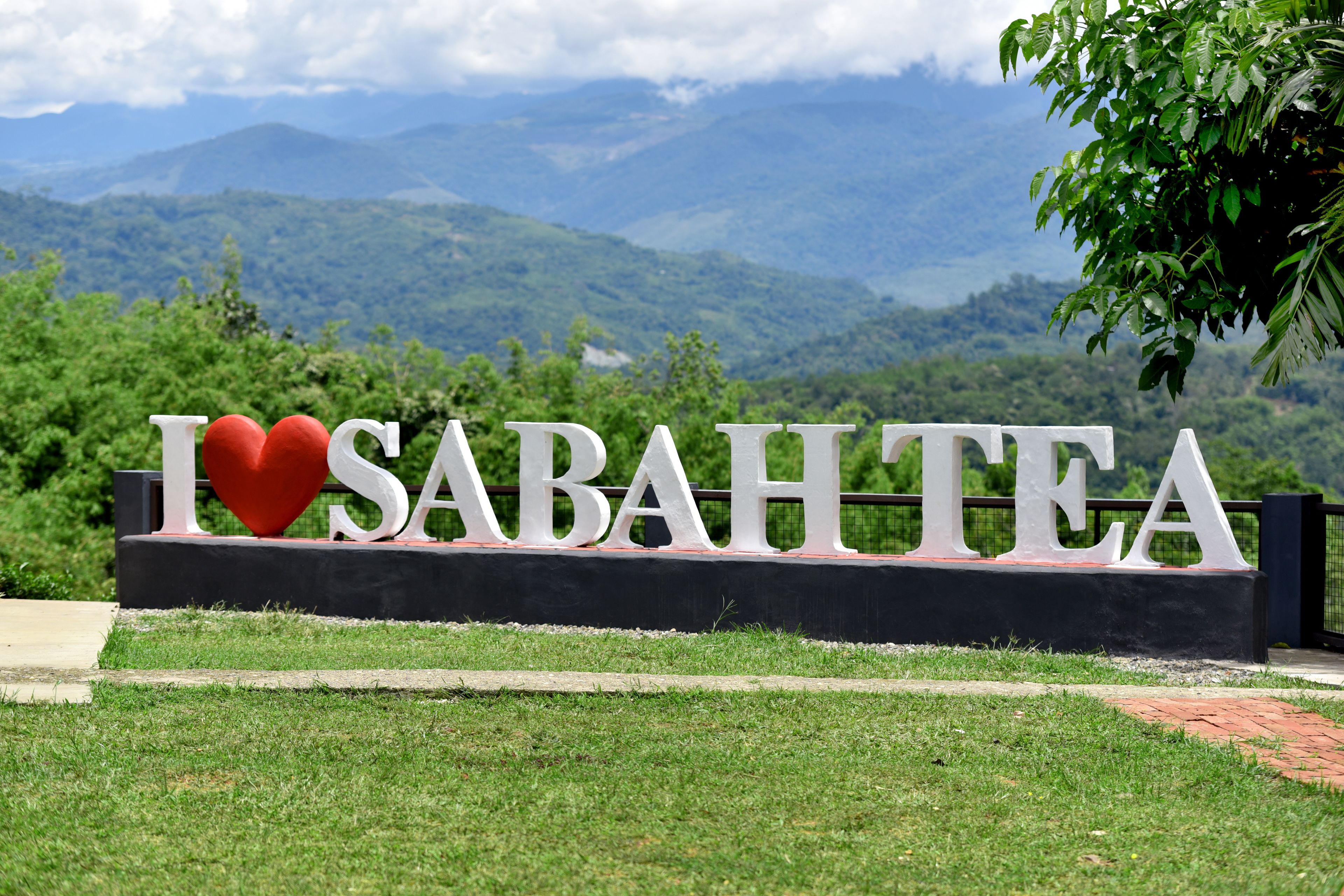 A sign with the text "I ♥ SABAHTEA" set against a backdrop of lush green hills and mountains.