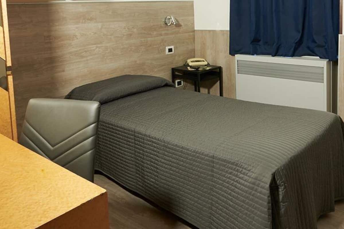 A compact hotel room with a bed, a small bedside table, a chair, and a desk.