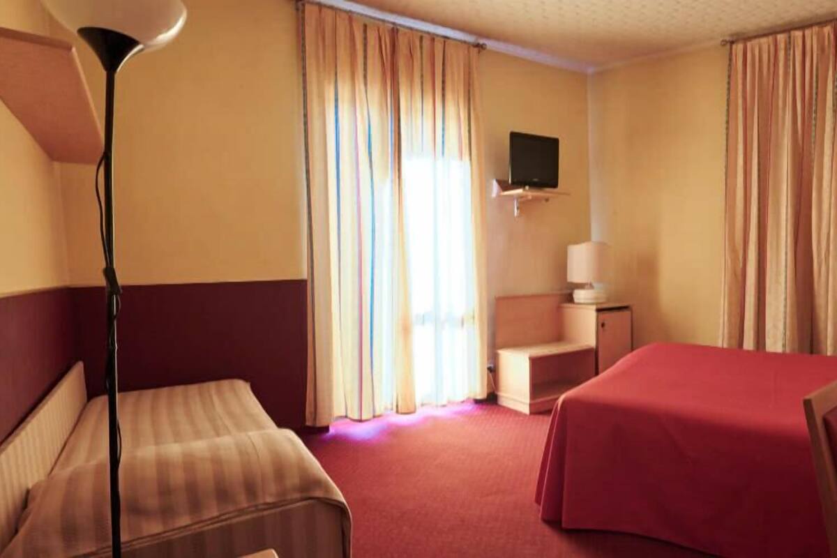 A hotel room with two beds, a desk, a chair, a TV, and curtains.