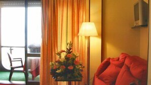 A hotel room with a red sofa, a table with a lamp, and a view through a glass door. - Hotel Atlantic (Arona)