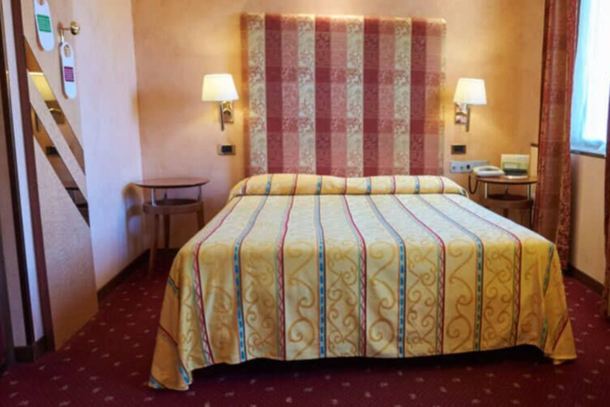 A hotel room with a bed, desk, chair, and two bedside lamps.