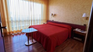 A hotel room with a bed, a small table, a nightstand, a lamp, and a window with curtains. - Hotel Atlantic (Arona)