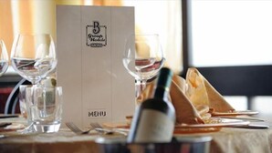 A restaurant setting with a menu stand labeled "B Group Hotels ARONA MENU" and a bottle of wine on the table. - Hotel Atlantic (Arona)