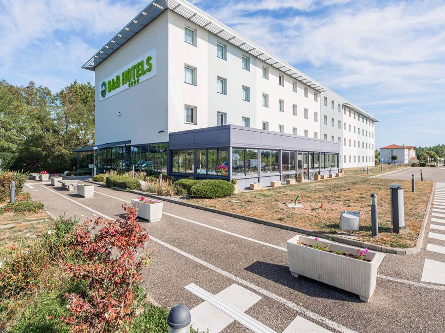 Un hotel moderno con gran fachada de vidrio, estacionamiento y jardines ajardinados.