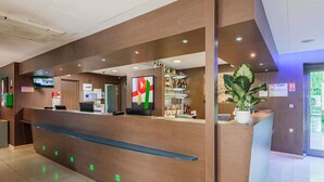 A modern reception desk with a digital screen, a bar area with shelves of bottles, and a large potted plant. - B&B HOTEL Colmar Liberté 4 étoiles (Colmar)