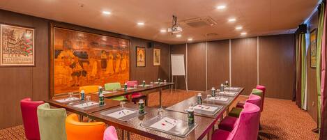 A conference room with a long table, colorful chairs, and a projector screen.