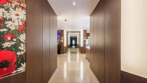 A hotel corridor with wooden paneling, a tiled floor, and a security camera on the ceiling. - B&B HOTEL Colmar Liberté 4 étoiles (Colmar)