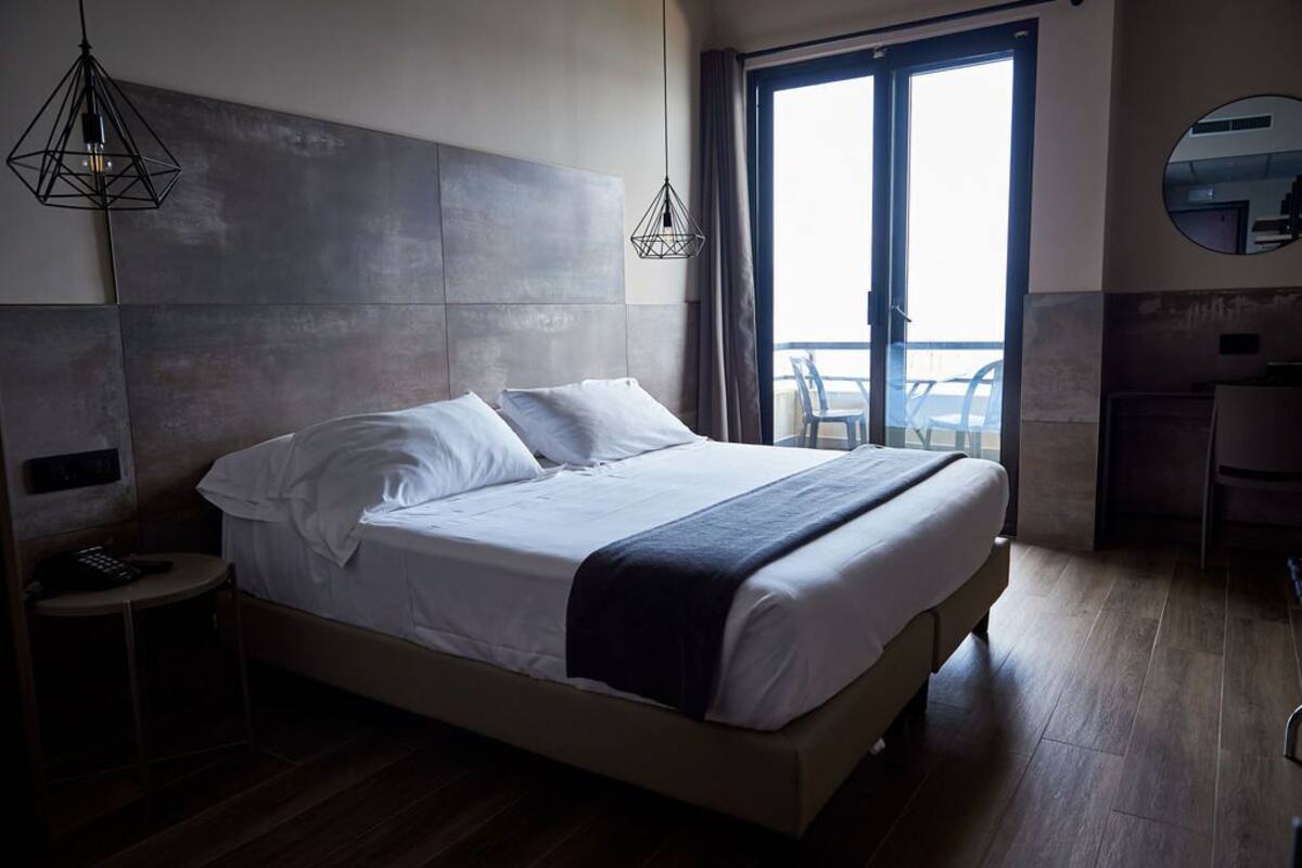 Una habitación de hotel moderna con una cama grande, una mesita de noche con teléfono y vistas al balcón.