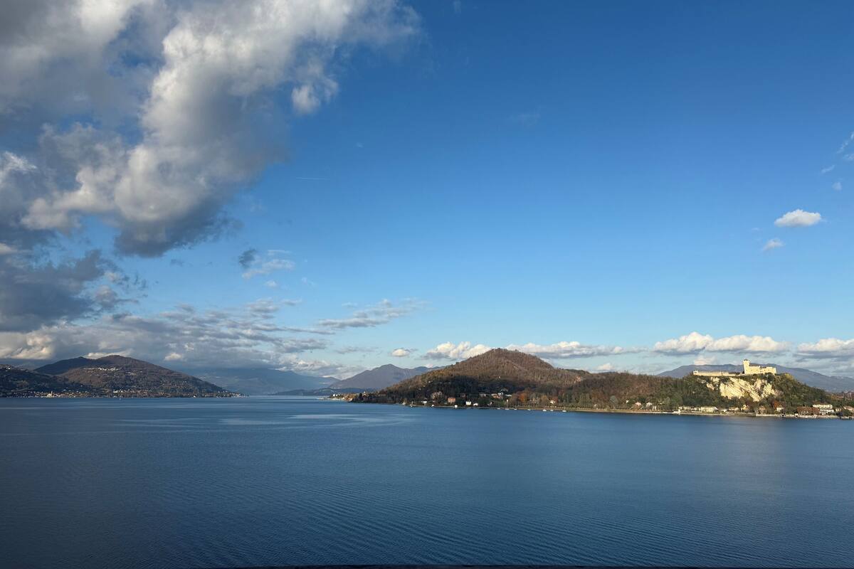 Un lago tranquilo con un castillo en una colina, rodeado de montañas y un cielo despejado.