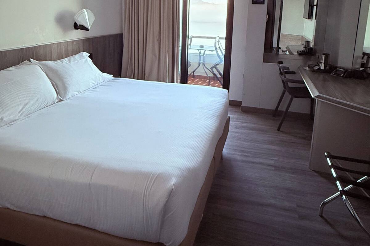 Habitación de hotel con una cama grande, un escritorio, una silla, una ventana con cortinas y vista a la playa.