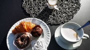 Un piatto con un croissant, un muffin e un donut ricoperto di cioccolato, un bicchiere di latte e una tazza di caffè su un tavolo.