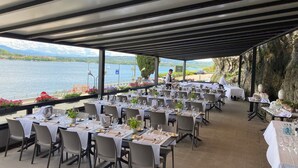 An outdoor dining area with tables set for a meal, overlooking a body of water and mountains. - Hotel Concorde (Arona)
