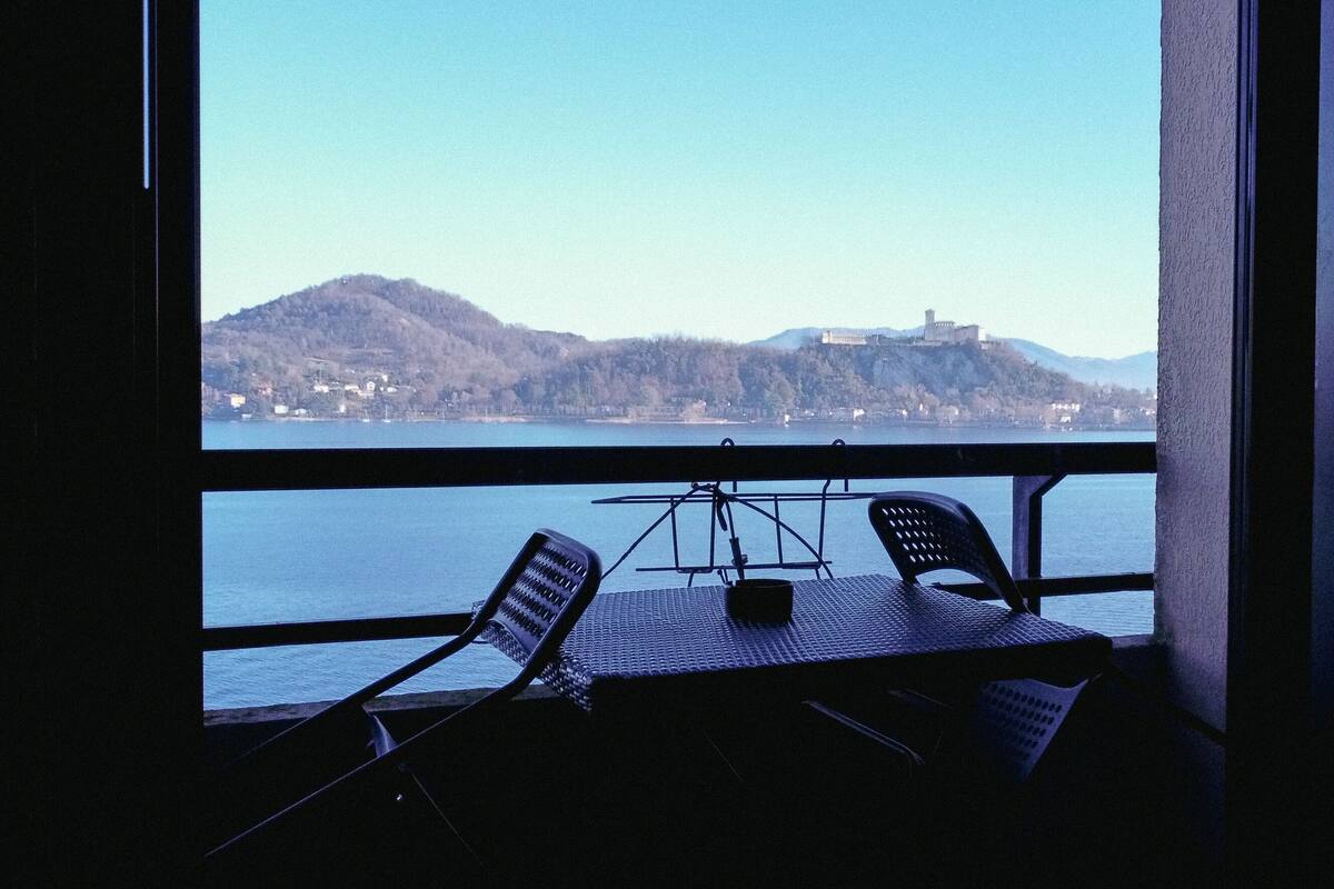 Un balcón con una mesa y dos sillas, con vista a un cuerpo de agua y una colina con un edificio.