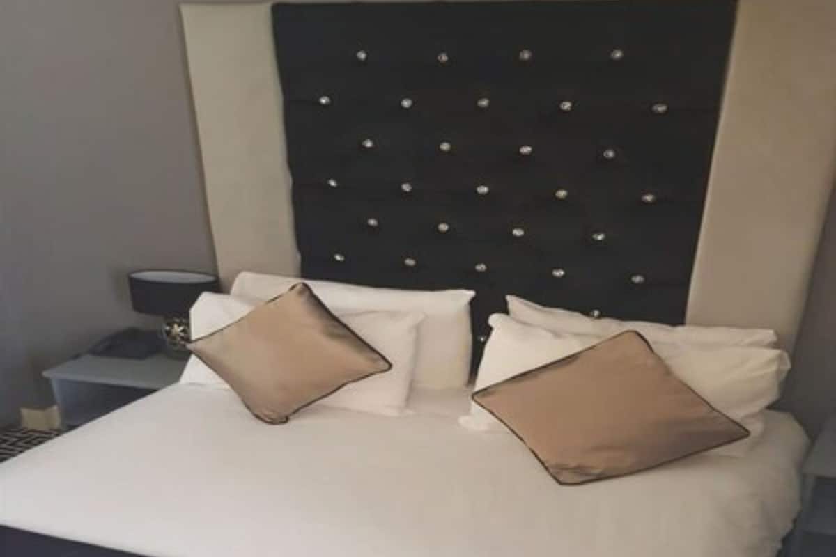 A neatly made bed with white and beige pillows, a black headboard with small decorative elements, and a bedside table with a lamp.