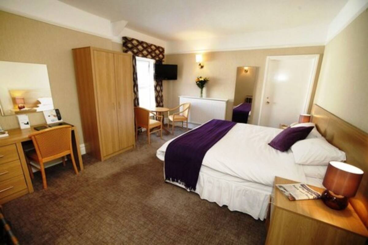 A hotel room with a bed, a desk, a chair, a wardrobe, and a TV.