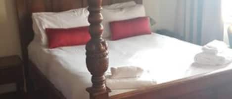 A four-poster bed with white linens and red pillows, a wooden headboard, and a red carpeted floor.