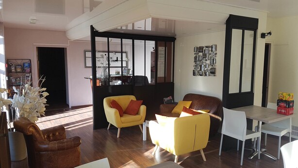 A modern living room with a yellow sofa, a brown leather armchair, and a white dining table. - Brit Hotel Le Surcouf (Saint-Malo)