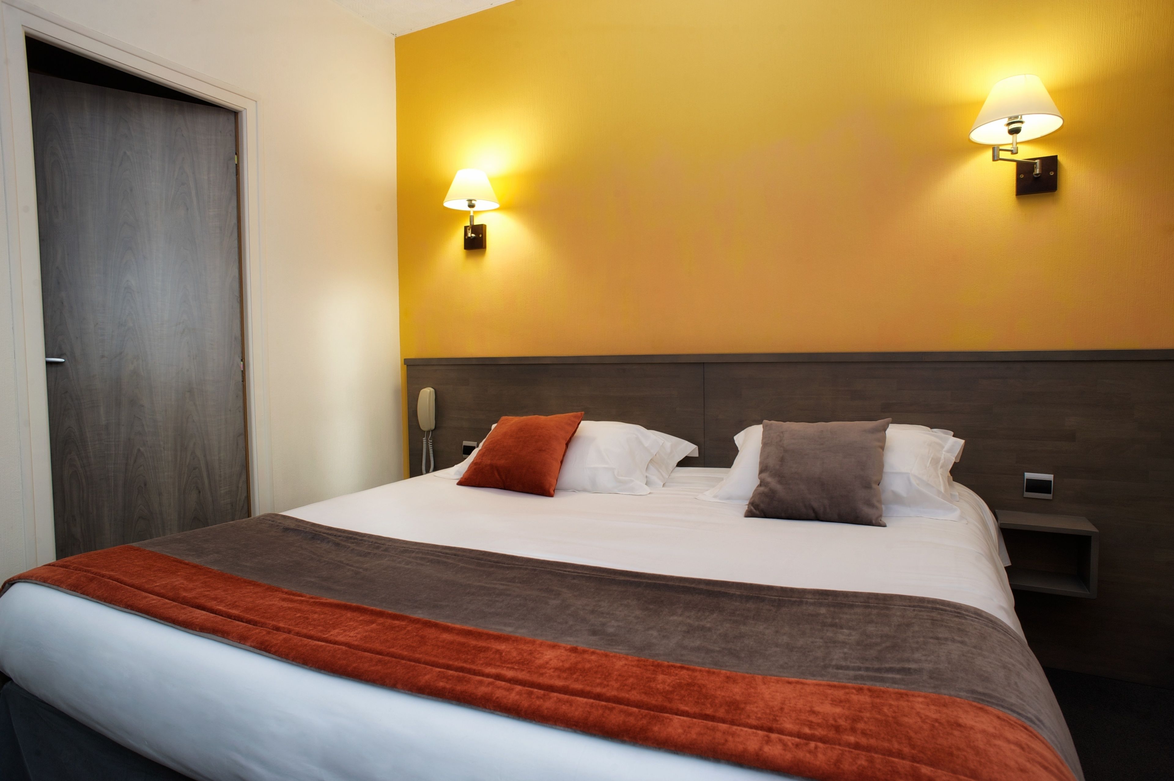 Habitación de hotel con una cama grande, dos lámparas fijadas a la pared, un cabecero de madera y una mesita de noche.