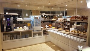 A modern café interior with a self-service coffee machine, various baked goods, and a display case. - Brit Hotel Le Surcouf (Saint-Malo)