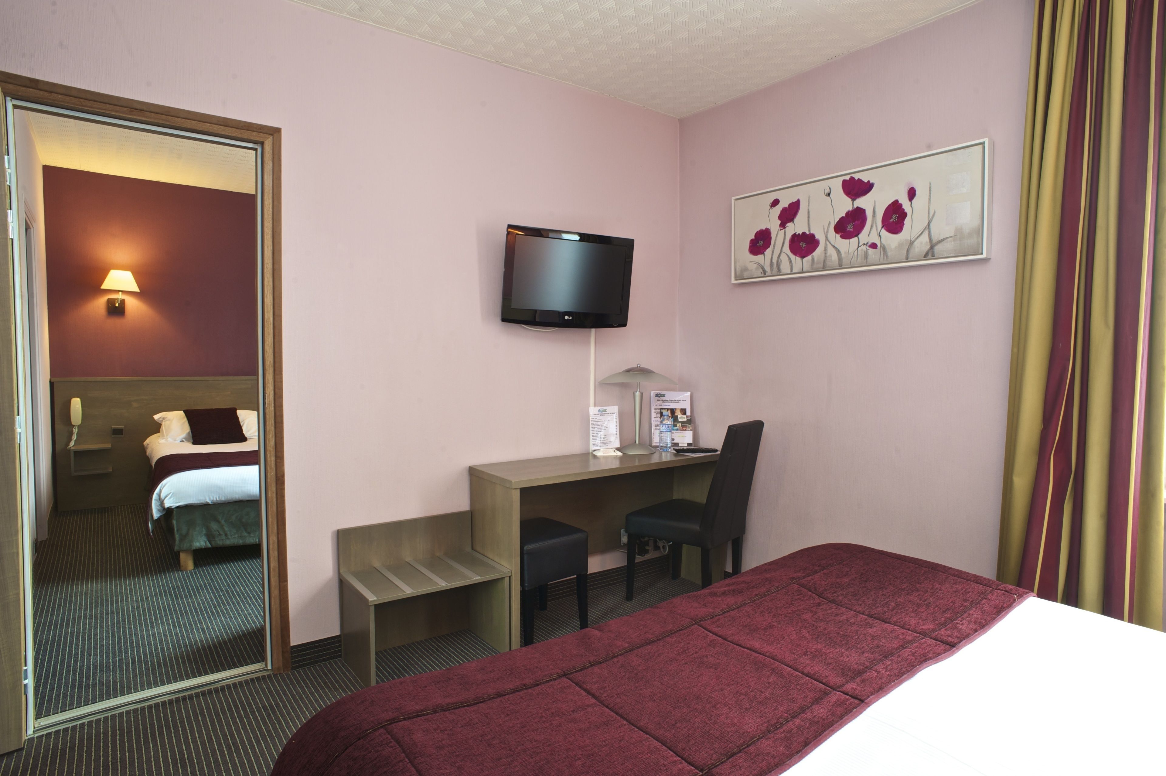 Una habitació d'hotel amb un llit, una taula, una cadira, una televisió i un quadre a la paret.