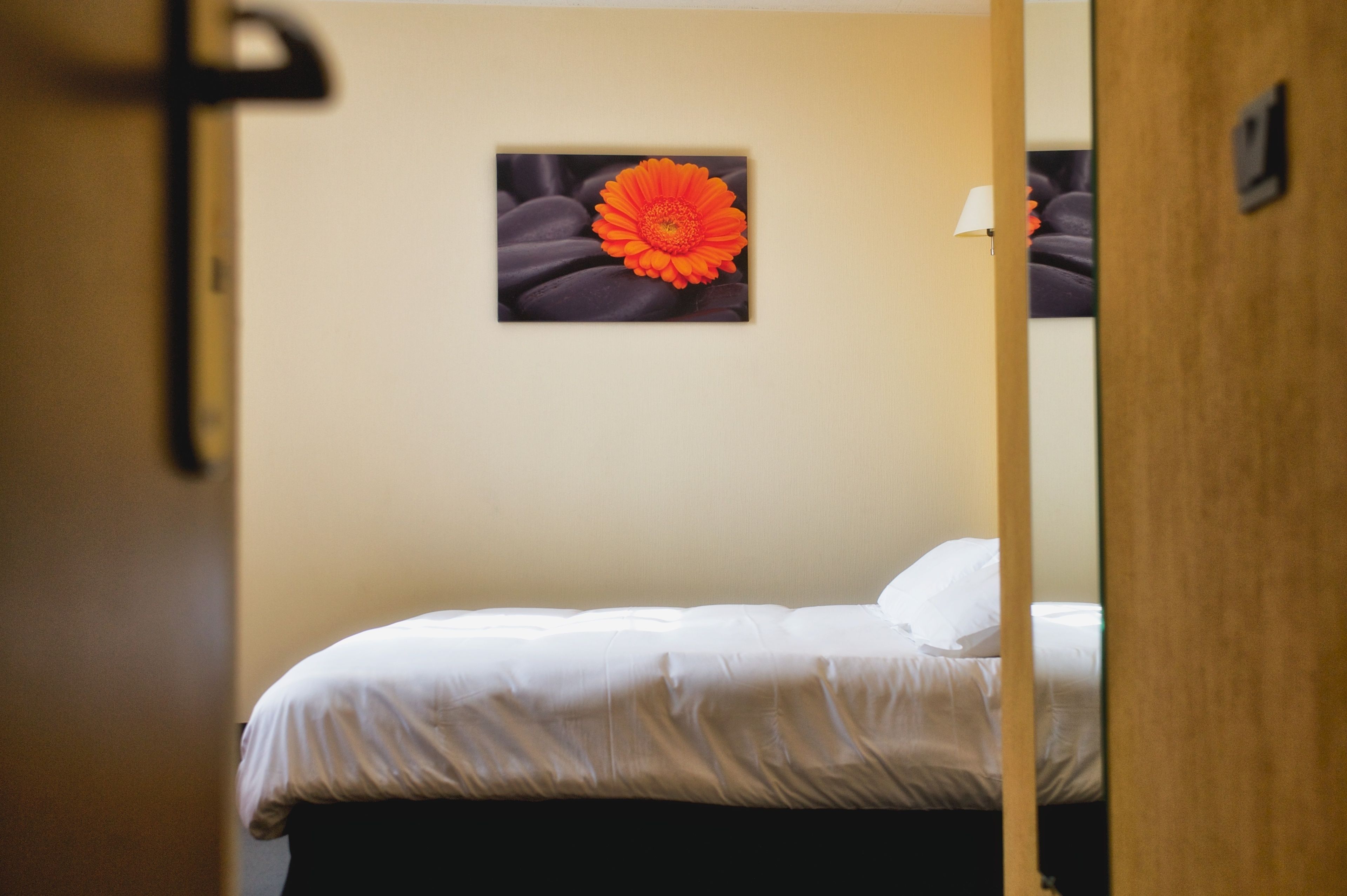 Una camera d'hotel con un letto, un quadro di un fiore appeso al muro e un telaio di porta.