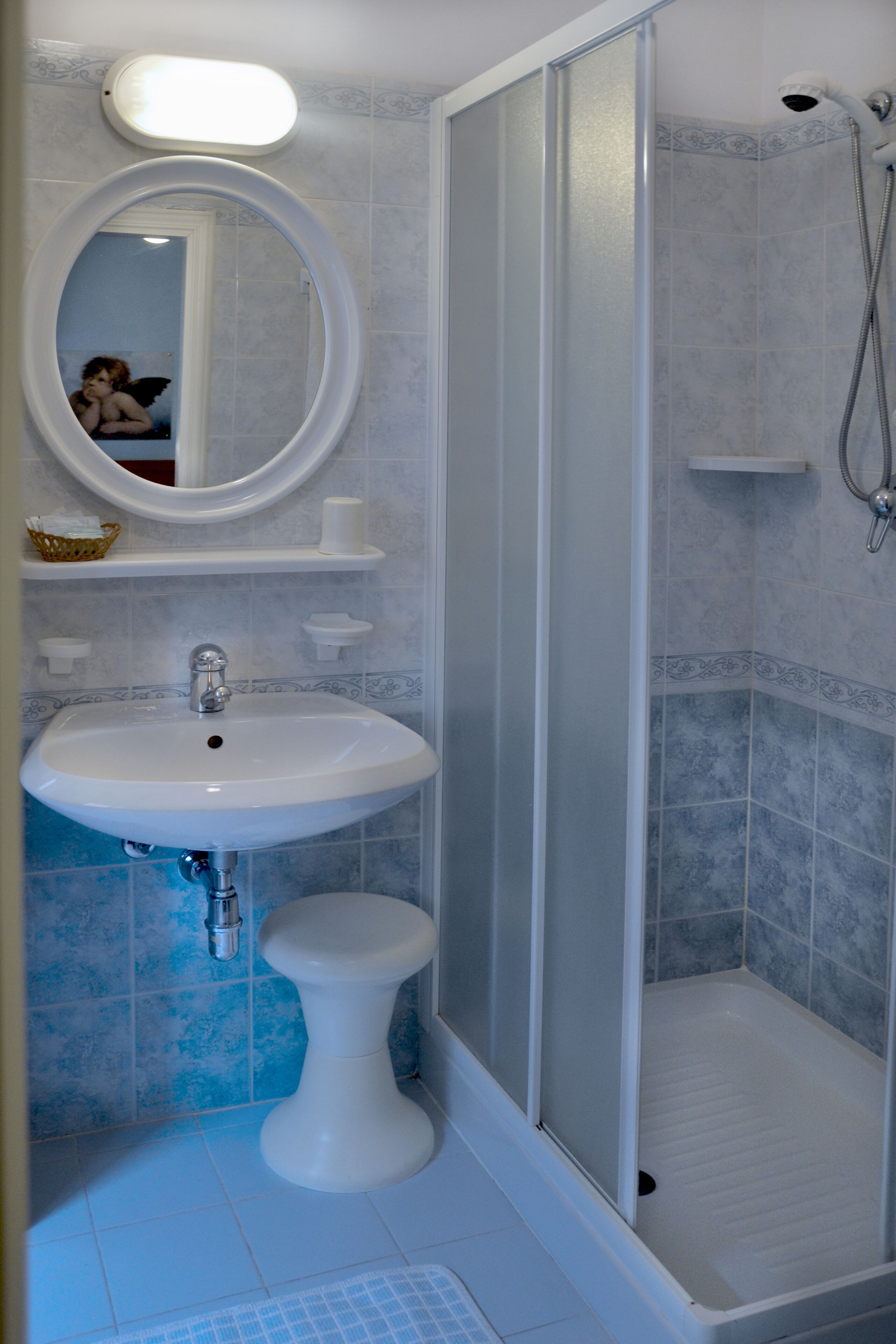 Un bagno con un lavandino su piedistallo, uno specchio, un box doccia e un pavimento piastrellato.