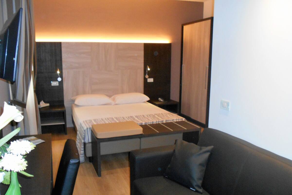 A modern bedroom with a bed, bedside tables, a TV, and a sofa.