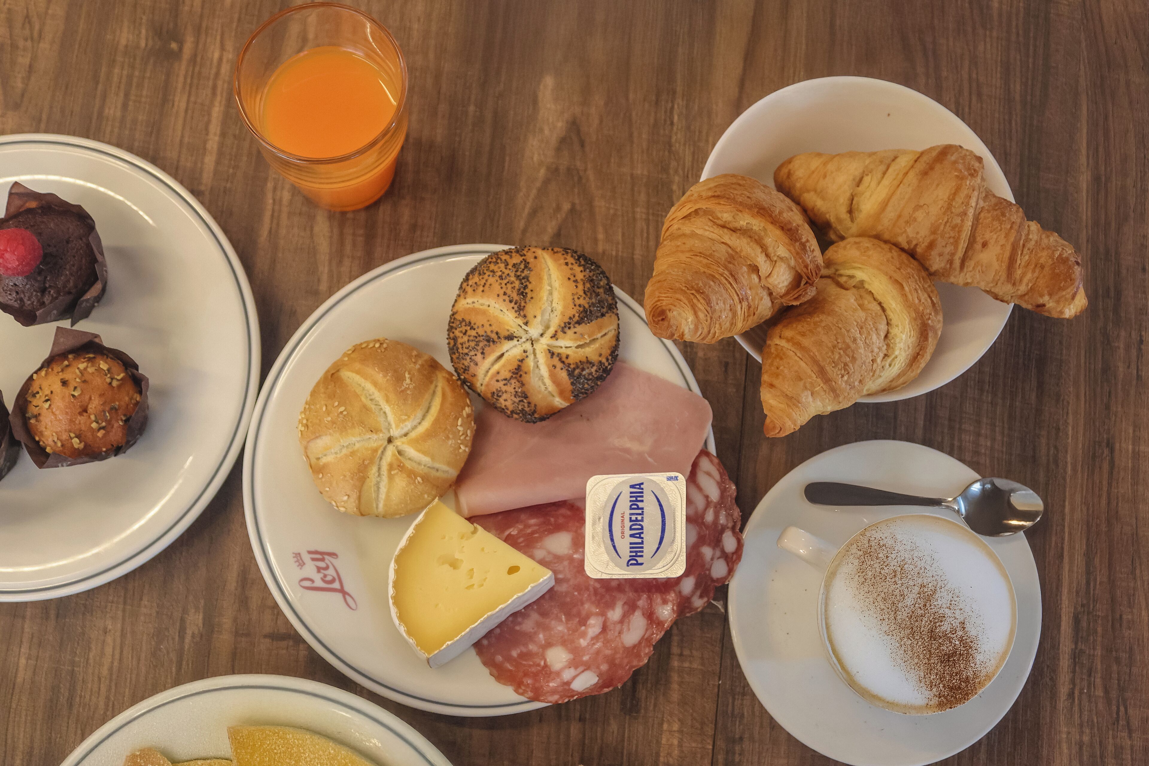 Taula de petit esmorzar amb croissants, formatge, salami i un got de suc d'aranja.