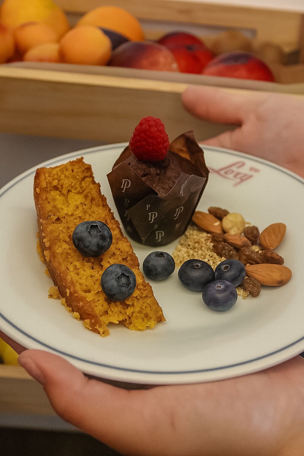 A plate with a slice of cake, a chocolate cupcake, blueberries, almonds, and a raspberry.