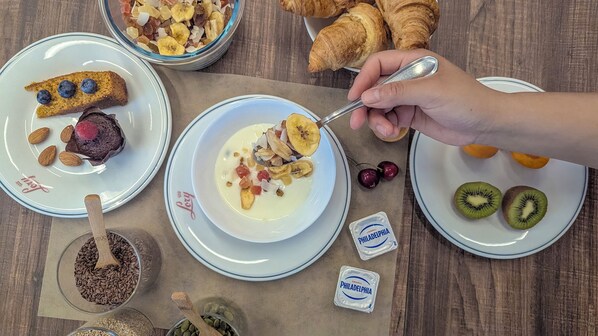 A breakfast setting with plates of food, including a bowl of cereal with fruits, a plate with a muffin and almonds, and a plate with kiwi slices. - Lory (Chianciano Terme)