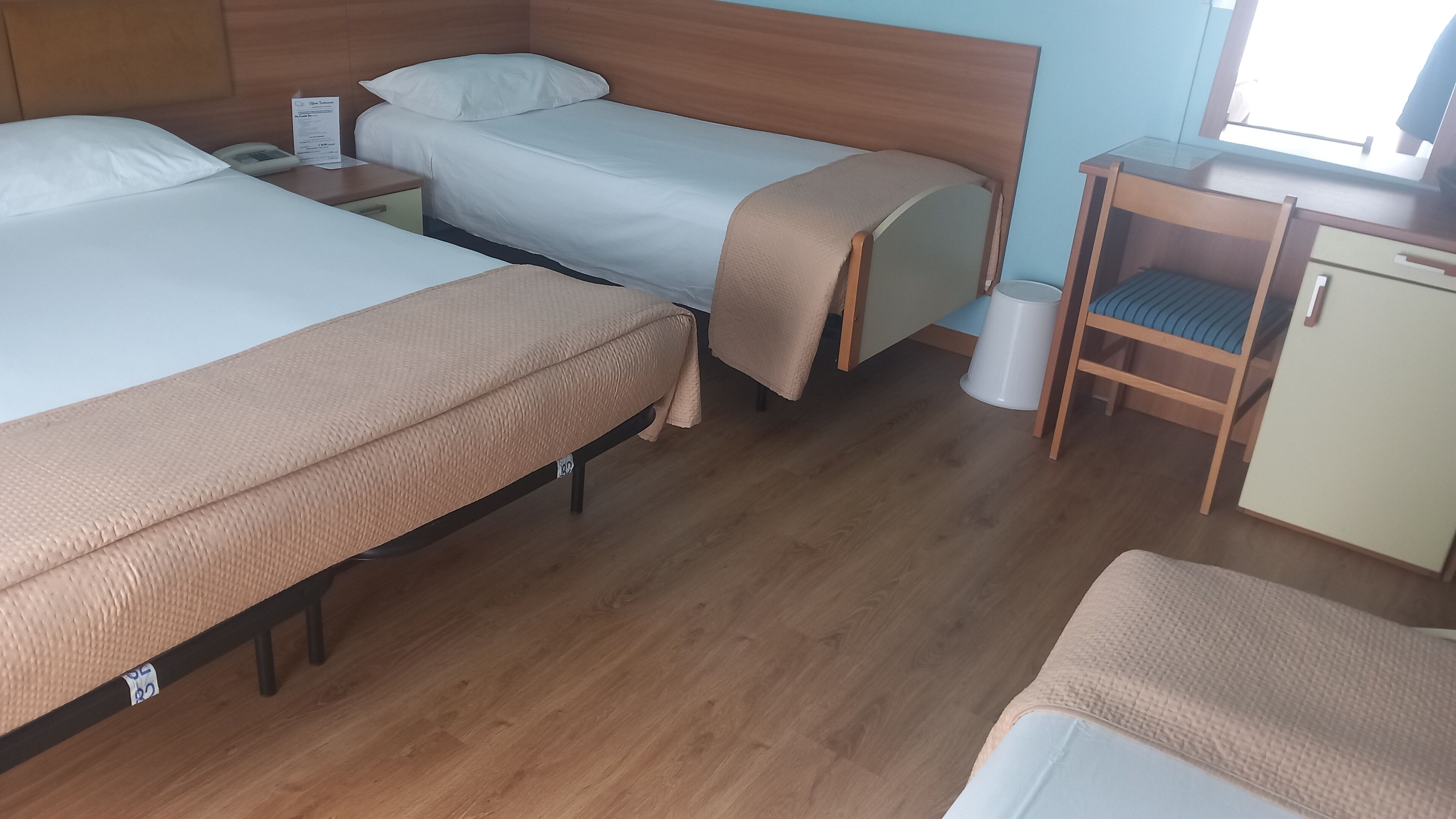 Une chambre d’hôtel avec deux lits, un petit bureau, une chaise et une poubelle.