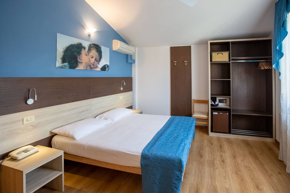 A hotel room with a bed, bedside table, and a wardrobe.