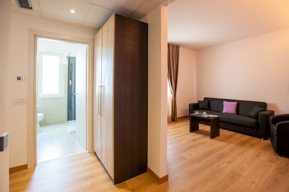 A modern living room with a dark-colored sofa, a wooden coffee table, and a view into the adjacent bathroom.