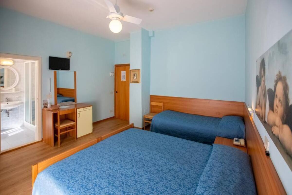 A bedroom with two beds, a wooden desk, a mirror, a television, and a ceiling fan.