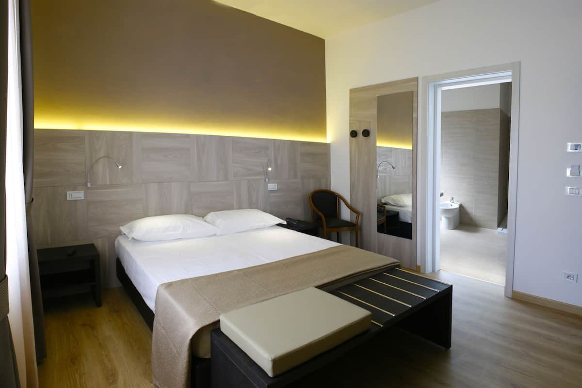 A modern bedroom with a bed, bedside table, and a mirror.