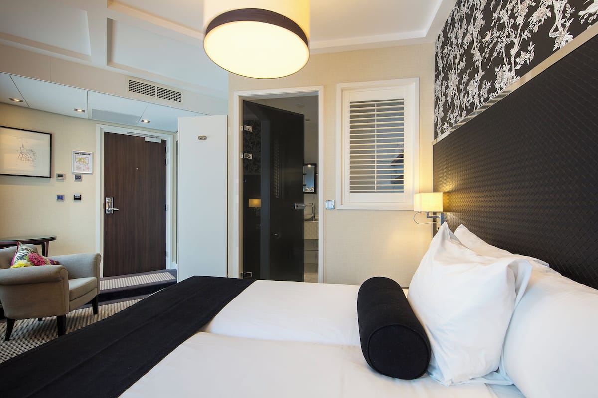 A hotel room with a bed, a chair, a desk, and a door leading to a bathroom.
