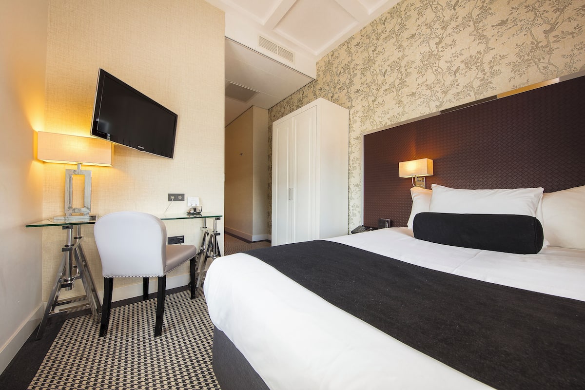 A hotel room with a bed, desk, chair, TV, and wardrobe.