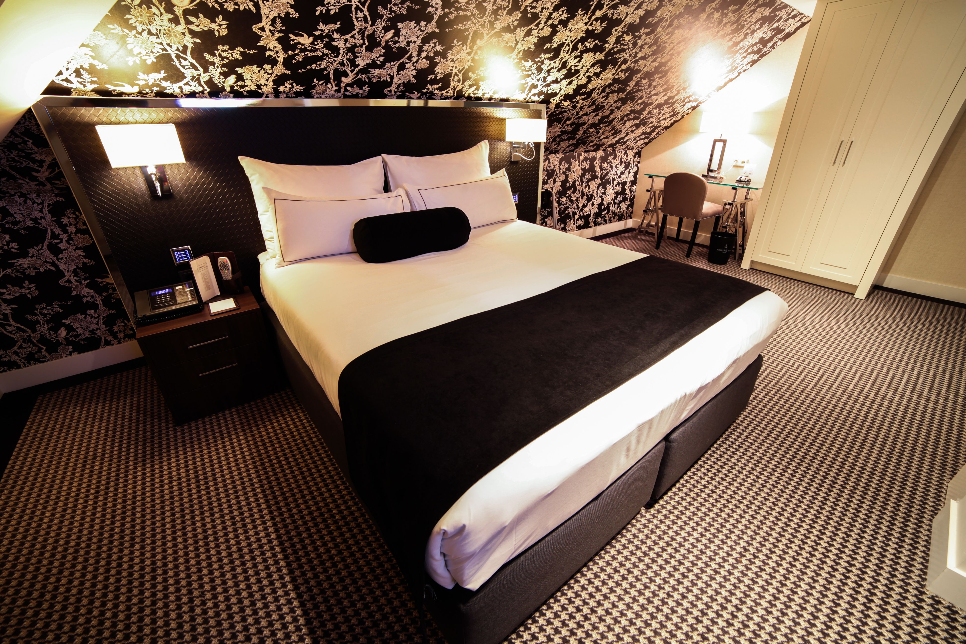 A hotel room with a large bed, a desk, and a wardrobe.