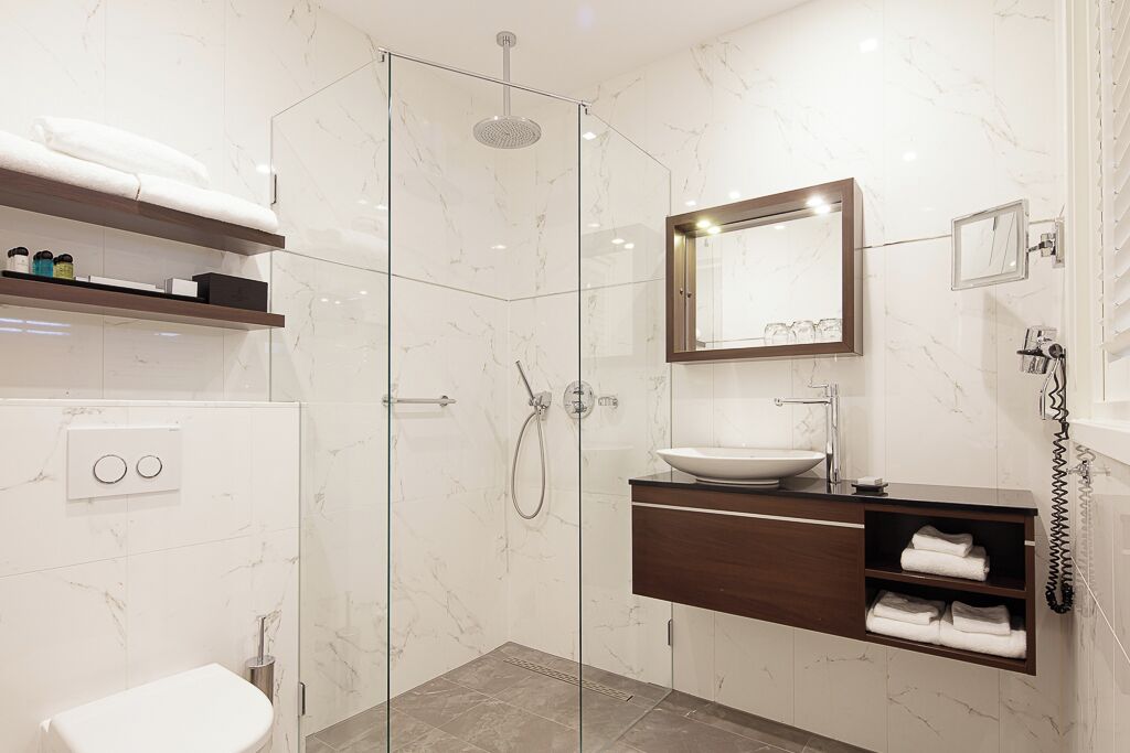 Un bagno moderno con cabina doccia in vetro, un lavandino bianco e un mobile bagno in legno.