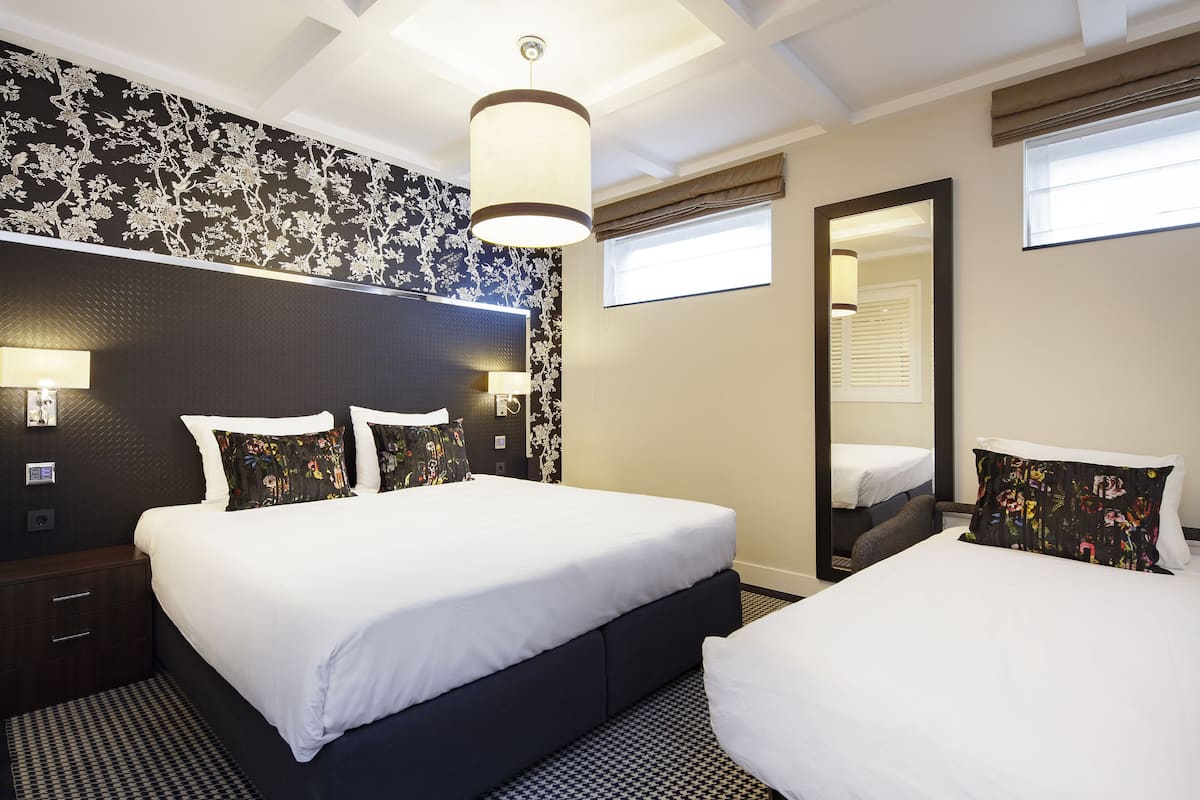 A hotel room with a large bed, a smaller bed, a nightstand, a mirror, and a window with blinds.