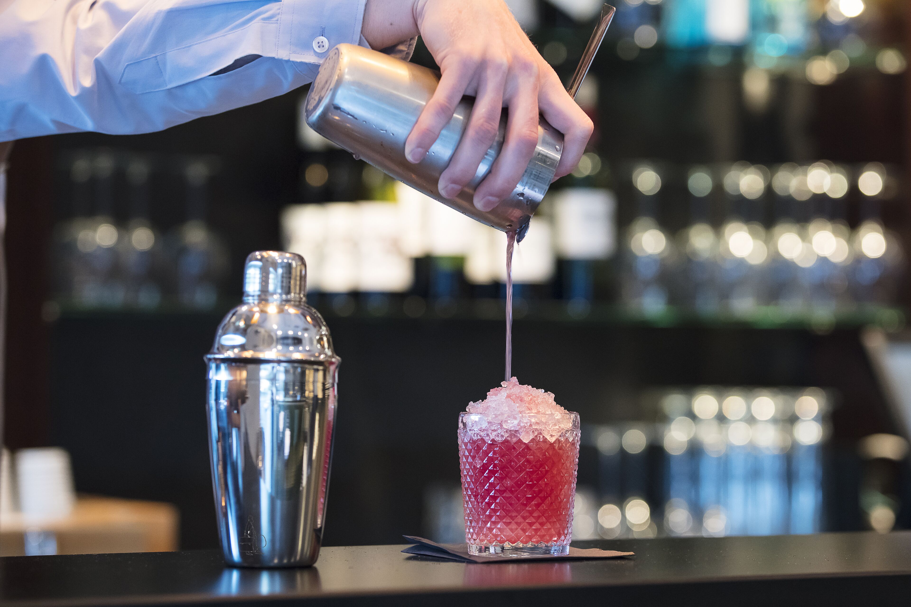 A bartender pouring a drink into a glass with ice.
