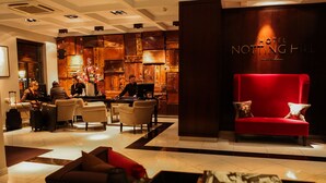 Vestíbulo de hotel con un sofá rojo, varios sillones, una recepción y una pared con el nombre del hotel.