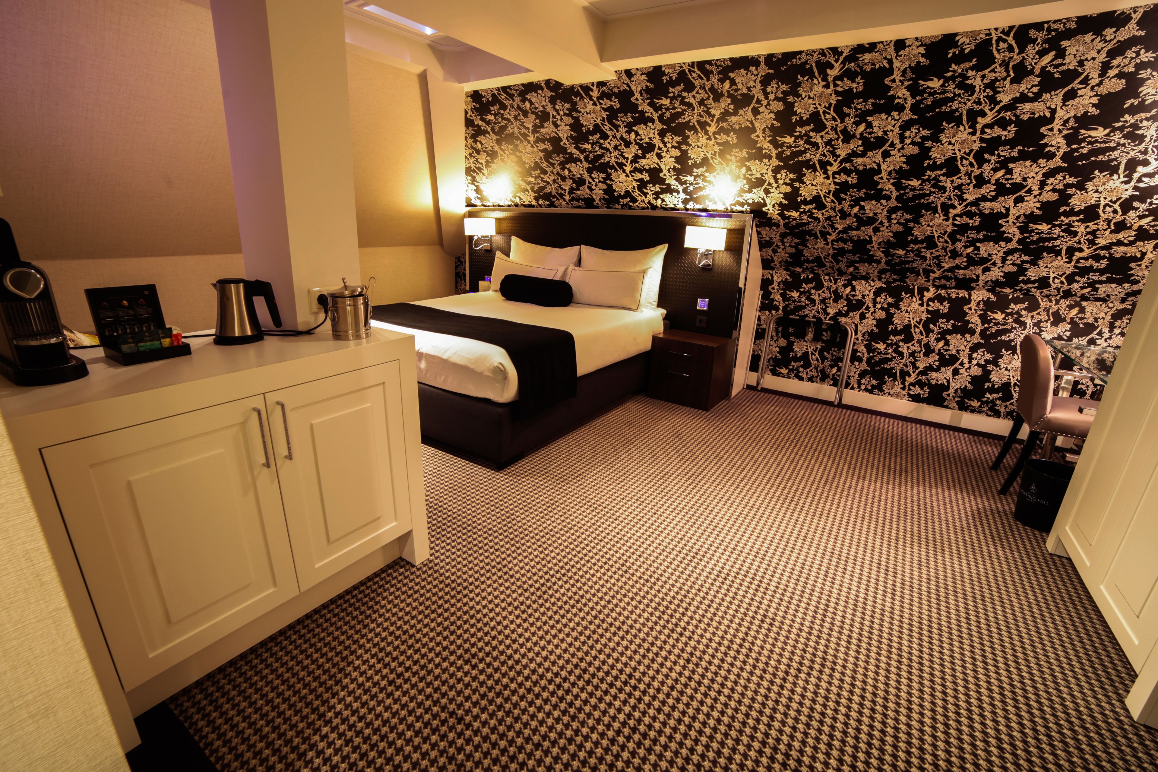 A hotel room with a bed, bedside tables, a wardrobe, and a patterned wallpaper.